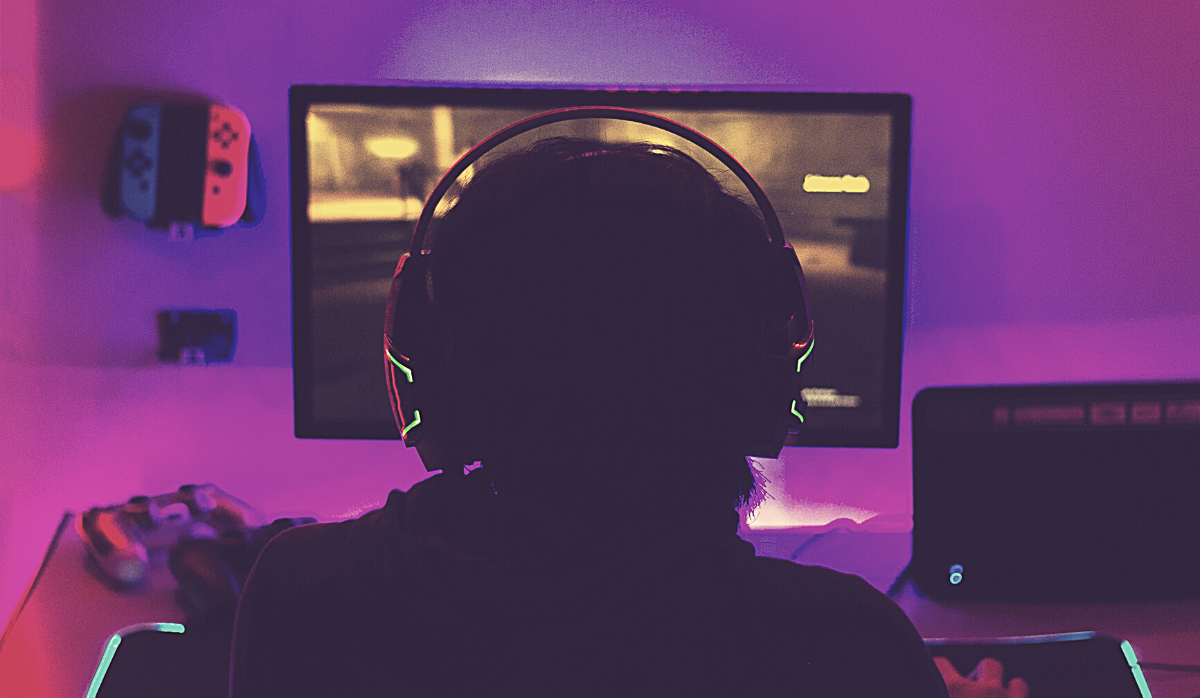 The back of someones head as they stare at a TV screen with a gamer headset on. The vibe is purple glow.