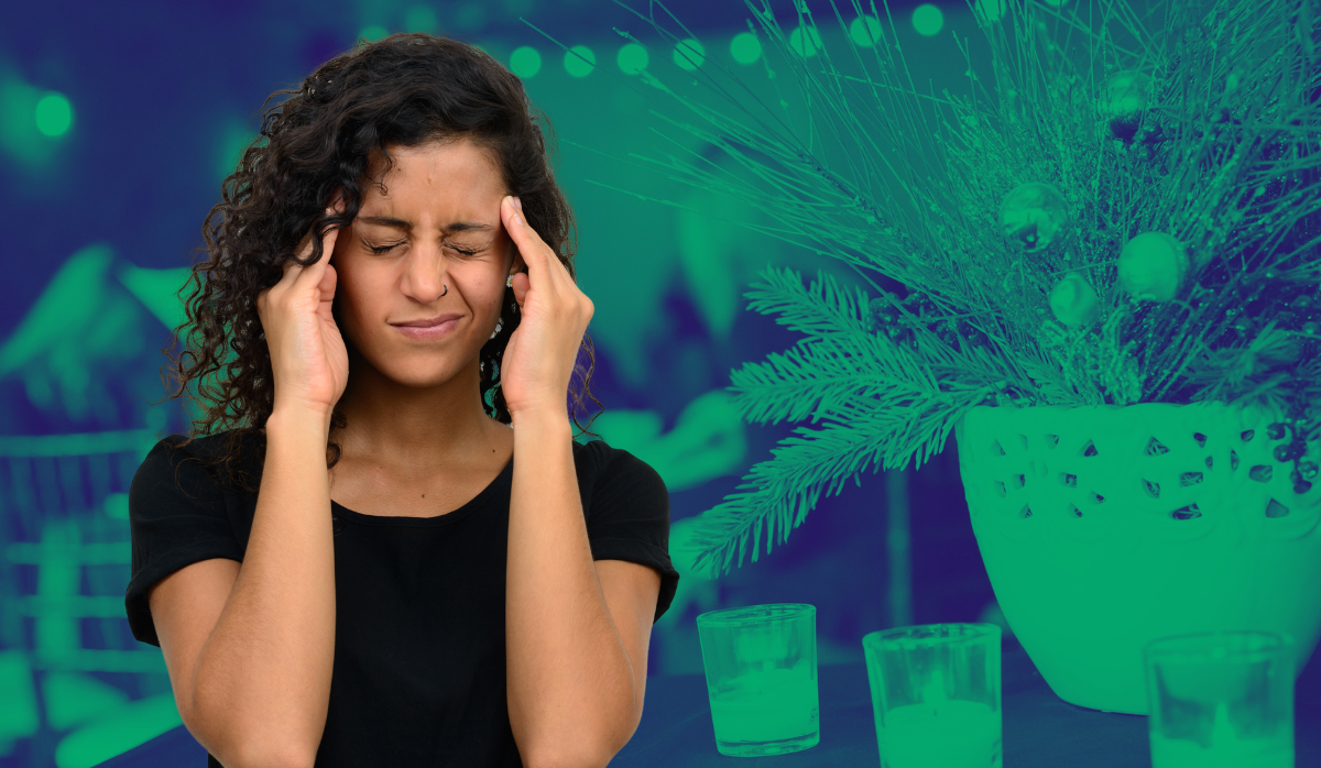 A stressed woman frowns and rubs her temples in front of a holiday party background.